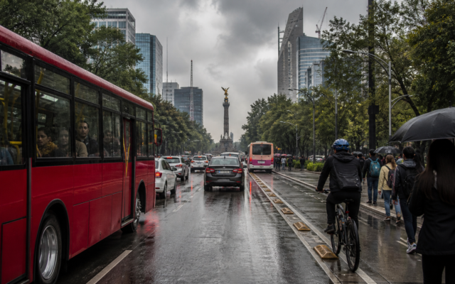 Avenida de Ciudad de México con tráfico bajo nubes de lluvia y pantallas de movilidad